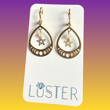 Load image into Gallery viewer, Gold teardrop earrings with star and moon designs on a Luster branded card against a gradient background.