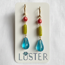 Load image into Gallery viewer, A pair of drop earrings displayed on a white Luster brand card against a white fabric background. Each earring has a gold fishhook clasp, a small faceted melon pink bead, a textured lime-green rectangular bead, and a larger translucent blue teardrop bead.