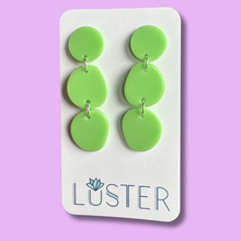 Load image into Gallery viewer, Green circular earrings on a Luster branded card against a purple background
