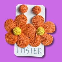 Load image into Gallery viewer, Orange flower-shaped earrings on a Luster branded card against a purple background
