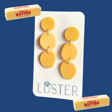 Load image into Gallery viewer, Yellow earrings on a Luster branded card with two blocks of butter on a blue background
