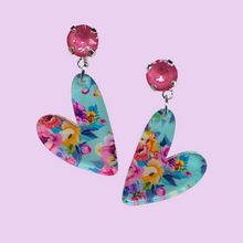 Load image into Gallery viewer, A pair of floral whimsical heart pendants on pink crystal studs, set on pale pink background.
