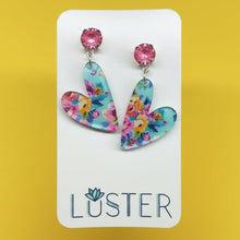 Load image into Gallery viewer, A pair of floral whimsical heart pendants on pink crystal studs, set on bright yellow background.
