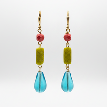 Load image into Gallery viewer, A pair of gold-tone dangle earrings featuring a faceted melon pink bead, a textured olive-green rectangular bead, and a translucent blue teardrop bead, shown against a light gray gradient background.
