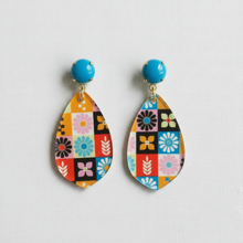 Load image into Gallery viewer, A pair of colorful teardrop-shaped dangle earrings with a retro patchwork floral pattern and bright blue round studs, displayed on a white textured fabric background.
