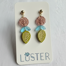 Load image into Gallery viewer, Pair of earrings with rose and leaf design on a Luster branded card.
