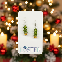 Load image into Gallery viewer, A pair of handmade dangle earrings shaped like pine trees, featuring green glass beads and small amber-colored accents, displayed on a white card with the brand name 'LUSTER'.
