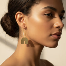 Load image into Gallery viewer, Pair of gold hoop earrings with arch-shaped pendants on a woman
